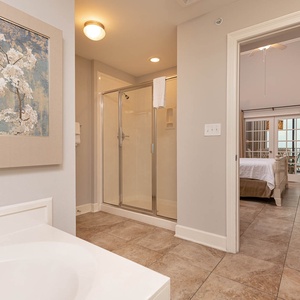 The master bath features a relaxing jetted tub, a glass walk-in shower, and a view into the elegant bedroom with soft decor
