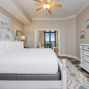 The master bedroom features a plush king bed, a wall-mounted TV, and a lovely view of the beachfront through large windows