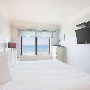This bedroom features a comfortable bed and stunning beachfront views from large windows, perfect for relaxation