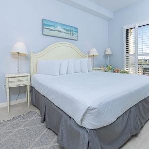 Master bedroom featuring a king bed with plush white linens, bedside lamps, and ground floor patio access