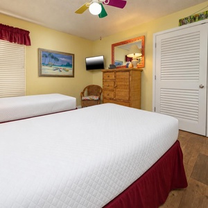 This bright guest bedroom features two twin beds, a wall-mounted TV, and beach-themed decor for a cheerful retreat