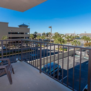 This balcony offers a relaxing spot with a chair, overlooking palm trees and the parking area, perfect for unwinding