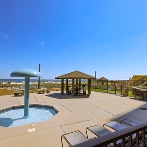 A playful water feature complements the spacious pool area, with picnic tables and a view of the beach just beyond