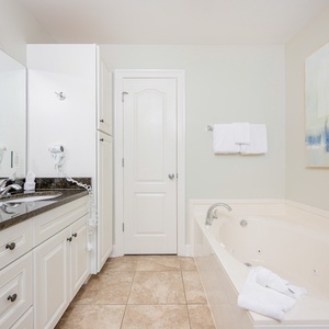 Relax in this master bathroom featuring a jetted tub, walk-in shower, sleek granite countertops, and modern white cabinetry