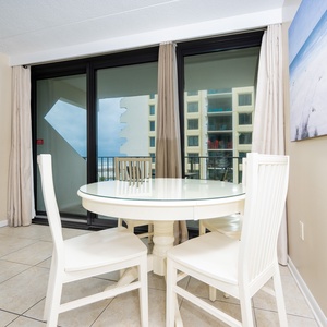 The dining area features a round table with white chairs and a view of the beach through large sliding glass doors