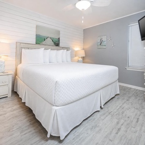 Bright and airy bedroom featuring a king bed, bedside lamps, a mounted TV, and coastal-themed decor for a relaxing retreat