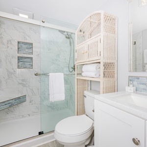 This bathroom features a sleek glass shower, elegant marble tiles, and a stylish woven shelf for towels