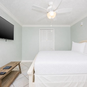 Cozy guest room featuring a queen bed, a wooden bench, and a wall-mounted TV for entertainment
