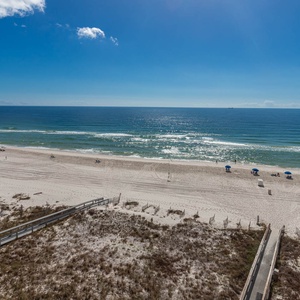 Expansive beachfront view reveals soft white sand and gentle waves under a clear blue sky, perfect for relaxation