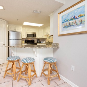 Kitchen area features a granite breakfast bar with three striped stools, white cabinetry, and modern appliances