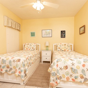 Relaxing guest bedroom featuring two twin beds with colorful shell-patterned quilts and cheerful yellow walls