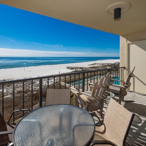 Spacious balcony featuring a glass table and chairs, offering a breathtaking view of the beach and tranquil blue waters