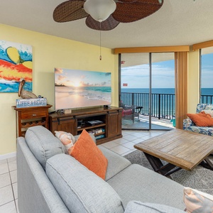 Brightly colored artwork complements the cozy living room, featuring a large TV and a stunning view of the beach