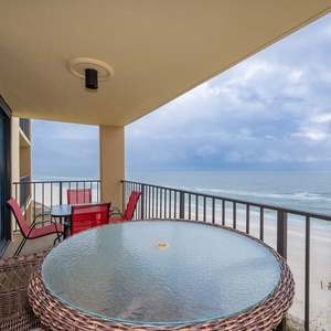 Enjoy breathtaking views from this balcony featuring a glass-top table and vibrant red chairs, perfect for relaxation