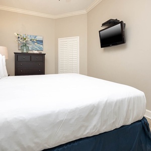 This cozy bedroom features a plush white king bed, a mounted TV, and tasteful decor, creating a relaxing retreat