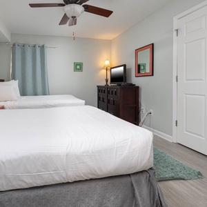 This guest bedroom features two full beds, a flat-screen TV, and soft blue accents for a relaxing atmosphere