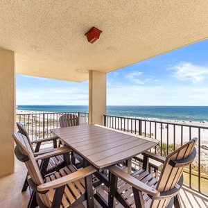 The balcony features a spacious table with seating, offering a delightful view of the beach and vibrant blue waters