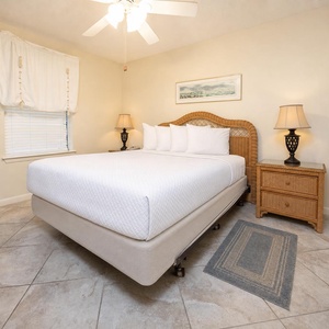 Bright guest bedroom featuring a queen bed with plush white linens, wicker accents, and soft lighting from bedside lamps