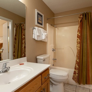 The bathroom features a light-colored tub/shower combo, a wooden vanity, and decorative striped curtains