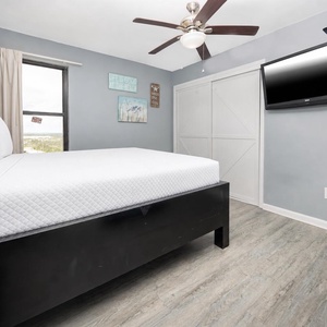 This cozy bedroom features a comfortable queen bed, a mounted TV, and beach-themed decor, perfect for a relaxing getaway