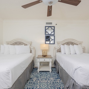 Two queen beds with plush white bedding and a decorative nightstand create a serene atmosphere in this guest bedroom