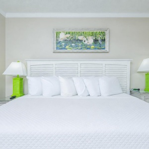 Rest comfortably in this guest bedroom featuring a king bed, bright linens, and cheerful coastal artwork above