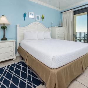 Cozy master bedroom featuring a king bed, light blue walls, and access to a balcony with a view of the beach