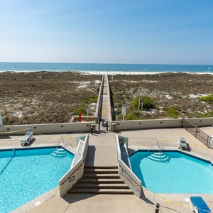Inviting pools overlook the beach, with a wooden walkway leading directly to the white sand and tranquil gulf waters
