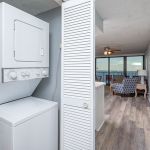 This laundry area features a stacked washer and dryer, with a view of the inviting living space and beachfront beyond