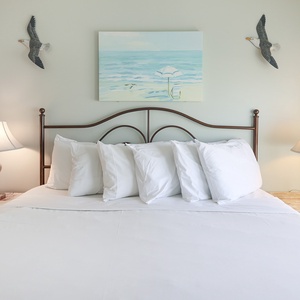 The bedroom features a comfortable bed with plush pillows and beach-themed decor, perfect for relaxation