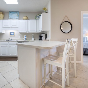 Bright white cabinetry and a breakfast bar with seating complement this modern kitchen, leading to the master bedroom