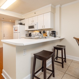 This kitchen features white cabinetry, essential appliances, and a breakfast bar with seating, perfect for casual dining