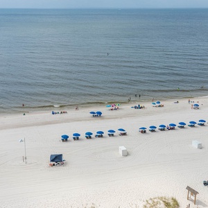 The view showcases a serene beach front with white sand and blue umbrellas, inviting relaxation and fun under the sun