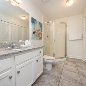 This extra bath features a sleek granite countertop, a glass shower, vibrant artwork, and laundry closet for convenience