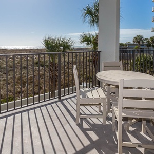 Outdoor seating area with a round table and chairs, offering views of the beach and gulf beyond the lush landscape