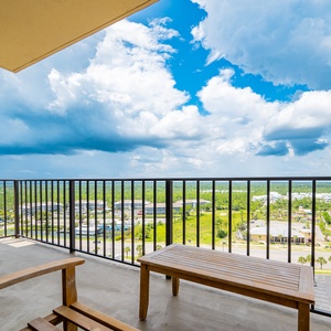 Enjoy breathtaking views from this spacious balcony, complete with a wooden bench and a vibrant blue sky overhead