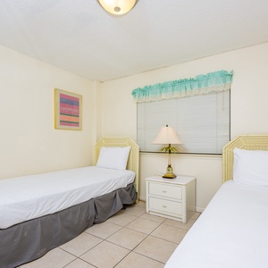 This bright room features two twin beds, colorful artwork, and a cozy lamp, perfect for a restful stay