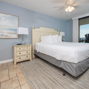 Brightly decorated master bedroom features a king bed, bedside lamps, and a sliding door leading to a balcony with seating