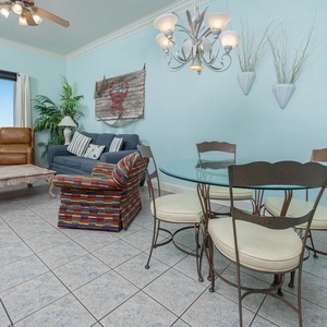 Living and dining area features a colorful chair, a blue sofa with queen sleeper, and a glass dining table