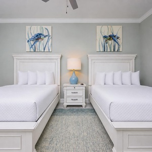 Rest comfortably in this serene guest bedroom featuring two queen beds, soft lighting, and charming artwork
