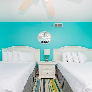 Vibrant turquoise walls complement two double beds, a stylish nightstand, and a colorful area rug in this guest bedroom