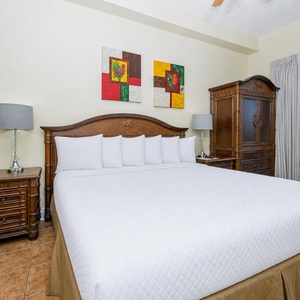 Brightly decorated master suite featuring a king bed, wooden furniture, and a sliding door leading to the patio