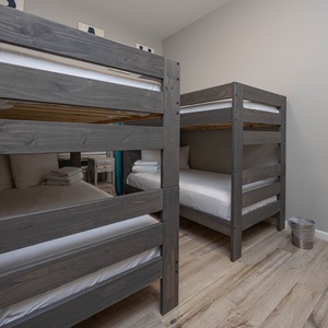 Two twin bunk beds with gray wooden frames create a fun sleeping space, complemented by soft linens and a warm wood floor