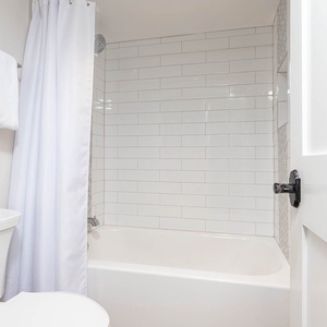 Master bathroom featuring a clean tub and shower combo, complemented by fresh white towels and modern tile accents
