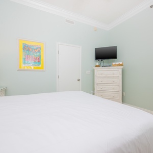 Brightly colored artwork complements the serene pastel walls in this cozy bedroom featuring a comfortable queen bed and TV