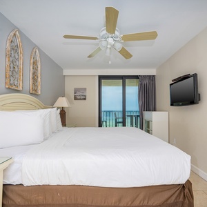 The master bedroom features a comfortable king bed, stylish decor, a flat-screen TV, and a lovely view from the balcony