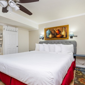 A spacious bedroom features a large king bed with white linens, decorative wall art, and a cozy area rug