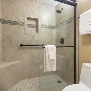 Experience a spacious walk-in shower with elegant tile work, a built-in seat, and plush towels for your comfort