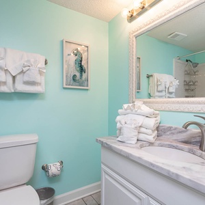 Bright turquoise walls complement the elegant marbled countertop and neatly arranged white towels in this inviting guest bath