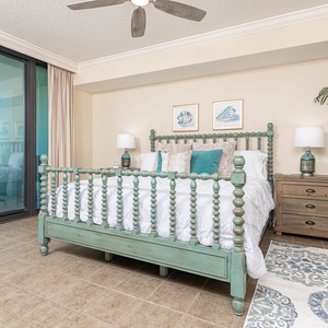 Unwind in the charming master bedroom featuring a teal king bed frame, soft linens, and a view from the balcony